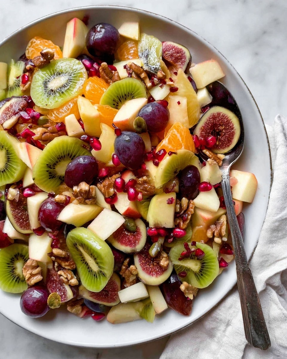 A large white plate filled with a colorful fruit salad that has many layers. The bottom layer shows thin slices of bright green kiwi with black seeds. On top are chunks of pale yellow apple, deep purple grapes, and orange segments of mandarin. Scattered throughout are halved ripe figs showing their textured pink flesh. Small red pomegranate seeds add a pop of brightness, along with green pumpkin seeds. There are also pieces of walnut and raisins for added texture. A silver spoon rests on the right side of the plate, partly submerged in the fruit mix. The plate sits on a white marbled surface with a light cloth partially visible on the right. photo taken with an iphone --ar 4:5 --v 7