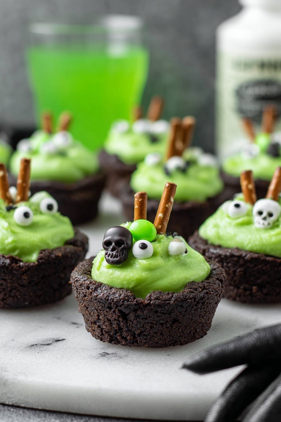 Cauldron Cookie Cups, Halloween cookie treats, spooky dessert ideas, chocolate cookie cups, festive party desserts - The image shows small dark brown cookie cups filled with bright green creamy frosting. Each frosting has small white and green candy decorations shaped like skulls and eyeballs, giving a spooky look. A small pretzel stick is inserted into the frosting on each cup, standing upright. The cookie cups are placed on a white marbled surface, and in the background is a blurry green drink and a white bottle with black text. A woman's hand in a black glove is reaching towards the cookie cups from the right side. photo taken with an iphone --ar 2:3 --v 7