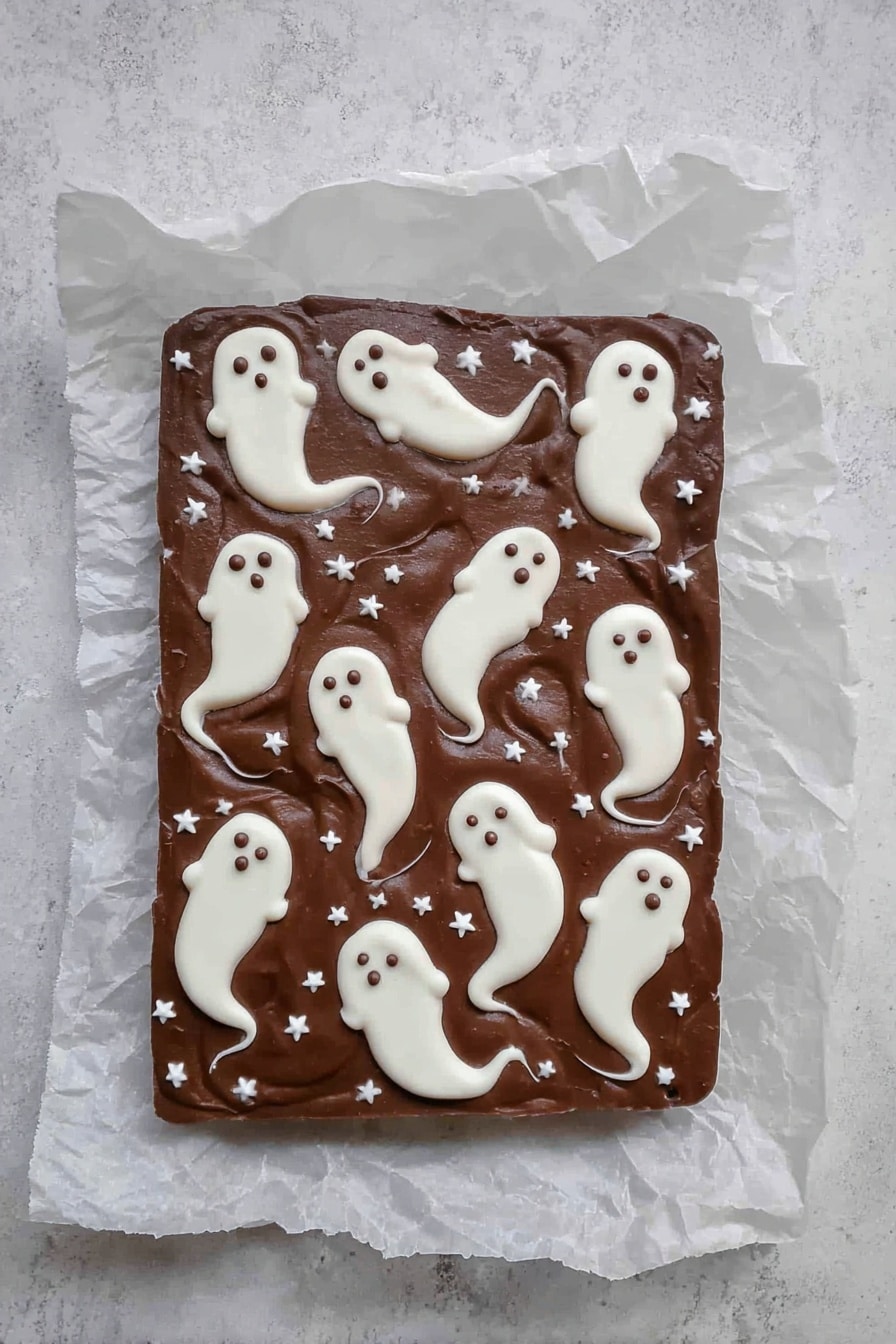 Halloween 3-Ingredient Ghost Bark, easy Halloween treats, quick Halloween dessert, festive ghost chocolate, simple Halloween candies - A rectangular chocolate fudge layer placed on crinkled white parchment paper on a white marbled surface, decorated with multiple small white ghost shapes spread across the top. The ghosts are made from a white creamy layer, each with rounded heads and flowing tails with small dark eyes and mouths, giving a spooky look. Small white star-shaped sprinkles are scattered evenly across the chocolate background, adding texture and contrast. The overall look is smooth with a few swirled edges on the ghost shapes, making a playful Halloween-themed treat. photo taken with an iphone --ar 2:3 --v 7