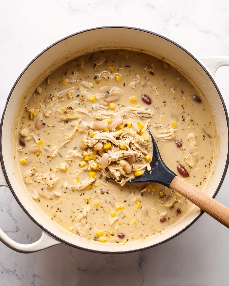 A large white pot filled with creamy beige soup, filled with shredded light-colored chicken, yellow corn kernels, and light and dark beans spread evenly throughout. A black spoon with a wooden handle is inside the pot, holding a scoop of the soup, showing its thick and chunky texture. The pot sits on a white marbled surface that contrasts with the warm color of the soup. photo taken with an iphone --ar 4:5 --v 7