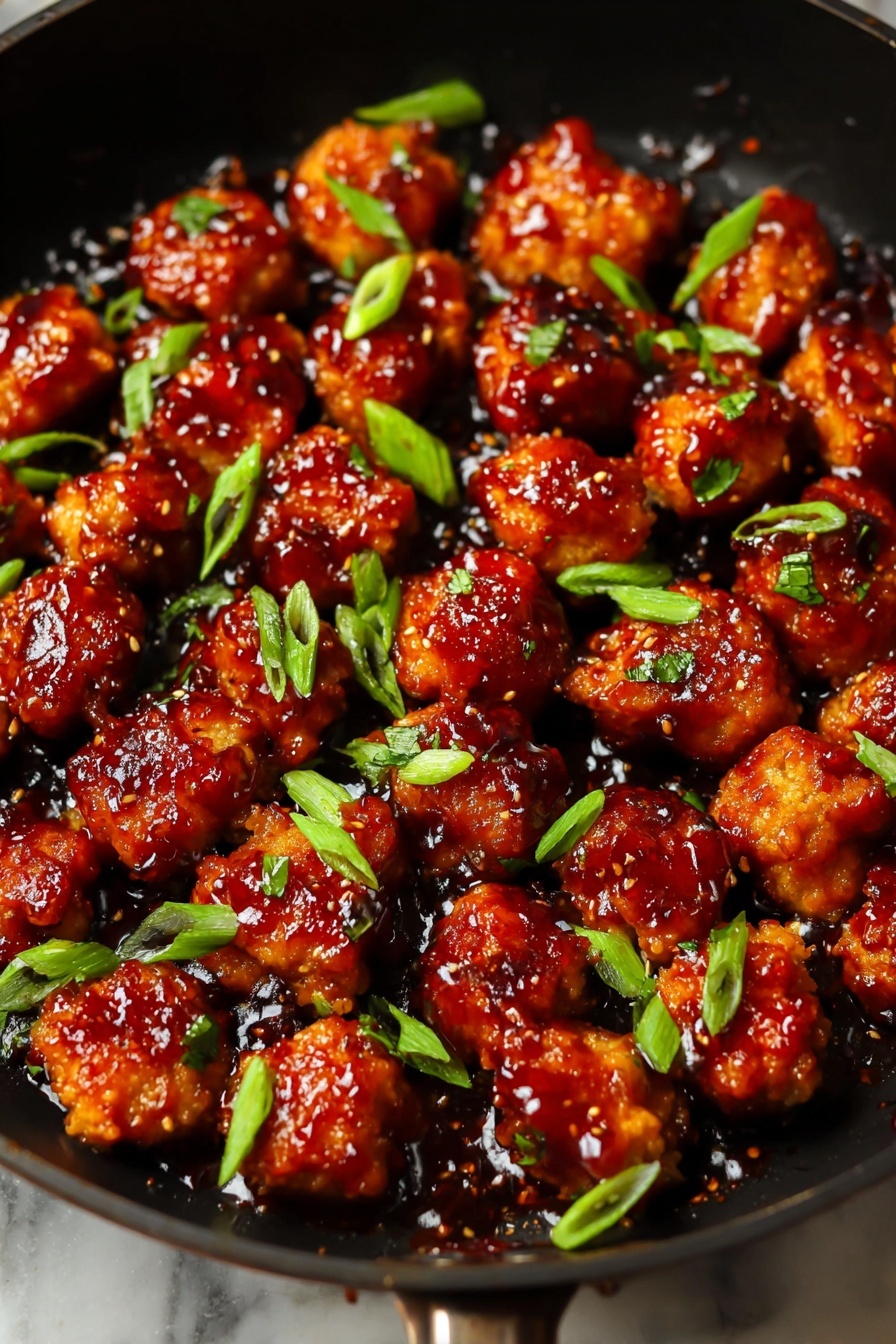 Honey Ginger Seitan with Crispy Pan-Fried Glazed Bites, vegan seitan recipe, plant-based honey ginger bites, crispy glazed vegan appetizer, savory vegan seitan dish - The image shows many small, round pieces of food in a black pan, each coated in a shiny, dark red sauce with a sticky texture. The pieces have a golden-brown color underneath the sauce, with some parts slightly charred. Scattered green slices, likely green onions, are placed on top, adding bright green spots across the pan. The pan’s surface has a glossy look with reflections from the sauce and slight oil shine, all set against a white marbled texture background. photo taken with an iphone --ar 2:3 --v 7