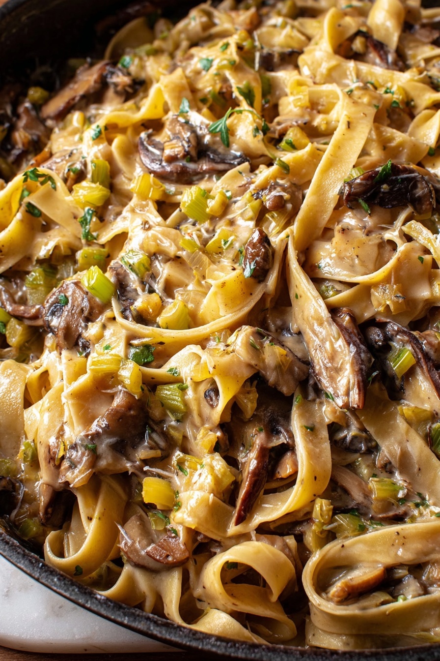 Caramelized Leek Mushroom Pasta, Leek Mushroom Pasta Recipe, Creamy Mushroom Leek Pasta, Vegetarian Pasta with Mushrooms, Gourmet Pasta with Gruyère - This close-up image shows a pan full of creamy pasta with broad, flat noodles tangled among large, uneven pieces of dark brown mushrooms. The sauce is light beige and coats the pasta and mushrooms, with small diced bits of green and yellow vegetables spread throughout, adding texture and color. The surface below the pan has a white marbled texture visible on the edges. photo taken with an iphone --ar 2:3 --v 7