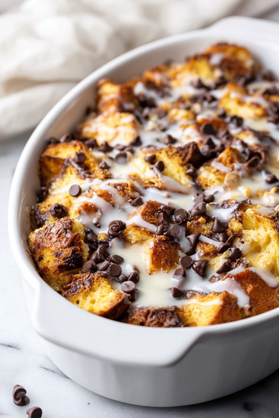 Tres Leches Bread Pudding with Chocolate Chips, tres leches bread pudding, bread pudding with chocolate chips, creamy tres leches dessert, indulgent bread pudding recipe - A white oval dish holds a baked bread pudding with layers of golden brown, toasted bread pieces that have a slightly crunchy texture, scattered generously with dark chocolate chips that add a rich contrast. The pudding is topped with a light drizzle of white glaze, giving a shiny and smooth finish. The dish sits on a white marbled surface with part of a soft white cloth in the background. photo taken with an iphone --ar 2:3 --v 7
