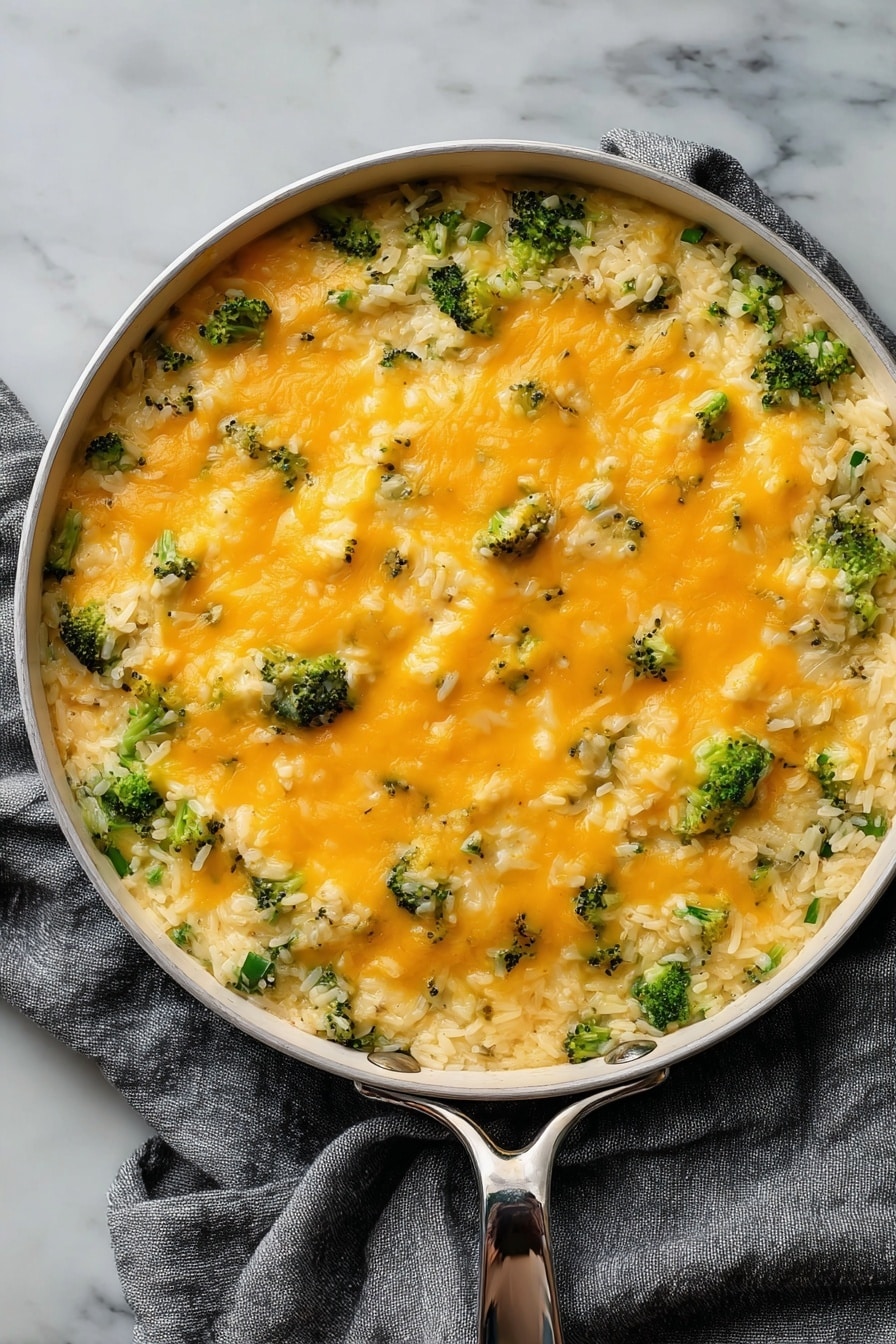 Cheesy Broccoli Rice Vegan Casserole, vegan cheesy broccoli casserole, dairy-free broccoli rice bake, plant-based broccoli casserole, healthy vegan rice and broccoli dish - The dish is served in a round white pan with a silver handle, placed on a gray cloth over a white marbled surface. It has two main layers: the bottom layer is a mix of cooked white rice with small pieces of broccoli, giving a textured base of green and white. The top layer is a smooth, even spread of melted orange cheese covering the rice and broccoli, with small bits of broccoli peeking through. The cheese looks soft and slightly shiny, adding a creamy contrast to the grainy rice below. photo taken with an iphone --ar 2:3 --v 7