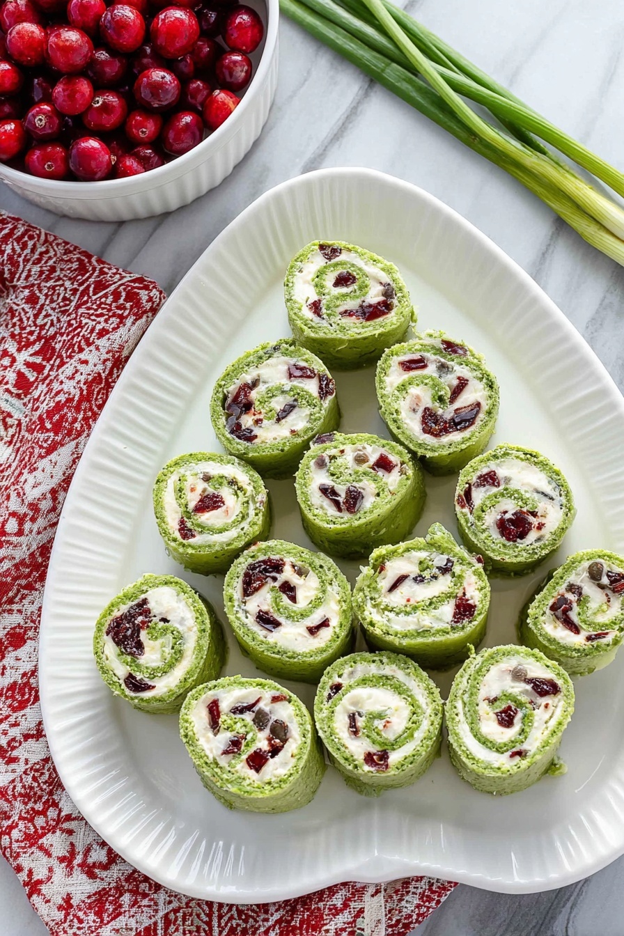 Cranberry Feta Spinach Tortilla Pinwheels, festive appetizer ideas, easy party snacks, healthy vegetable roll-ups, quick appetizer recipes - On a white oval plate with a ridged edge, there are fifteen green pinwheel rolls arranged in a triangular shape, with one at the top, three in the second row, five in the third row, and six in the bottom row. Each roll shows a swirl of bright green outer layer with a creamy white filling inside that contains small pieces of dark red and green ingredients mixed throughout. The plate is placed on a white marbled surface, and to the top left, a white bowl filled with red berries is partially visible, sitting on a red and white patterned cloth. A few green onion stems lie on the top right corner of the surface. Photo taken with an iphone --ar 2:3 --v 7