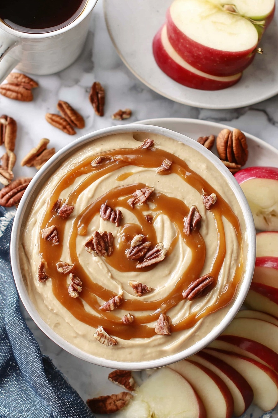 Caramel Cheesecake Dip, easy caramel cheesecake dip, creamy fruit dip, quick dessert dip, festive party dip - A white bowl holds a creamy beige dip that fills it nearly to the top, with smooth swirls of caramel sauce drizzled in a loose spiral on the surface. Small pieces of brown pecans are scattered evenly over the caramel, adding texture and contrast. Around the bowl, slices of red apple with white insides sit beside whole pecans. In the background, a white plate holds more apple slices, and a white marbled surface surrounds everything. A woman's hand holds a white cup filled with a dark drink near the top left corner. photo taken with an iphone --ar 2:3 --v 7