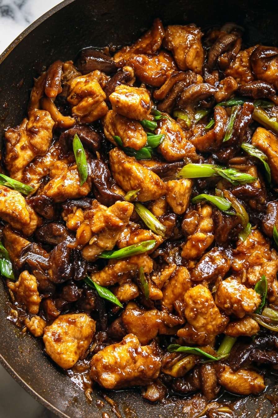 Black Pepper Mushroom Chicken Stir Fry, chicken stir fry recipes, mushroom stir fry, black pepper chicken, easy Asian stir fry - The image shows a close-up of a dark pan filled with a rich brown stir-fry dish. The stir-fry has several layers of golden brown cooked chicken pieces that look crispy on the edges, mixed with dark brown cooked mushroom slices. Scattered throughout the dish are small pieces of bright green sliced spring onions, adding a fresh contrast. The sauce covering the ingredients is glossy and thick, giving the dish a shiny look. The background is a white marbled texture. photo taken with an iphone --ar 2:3 --v 7