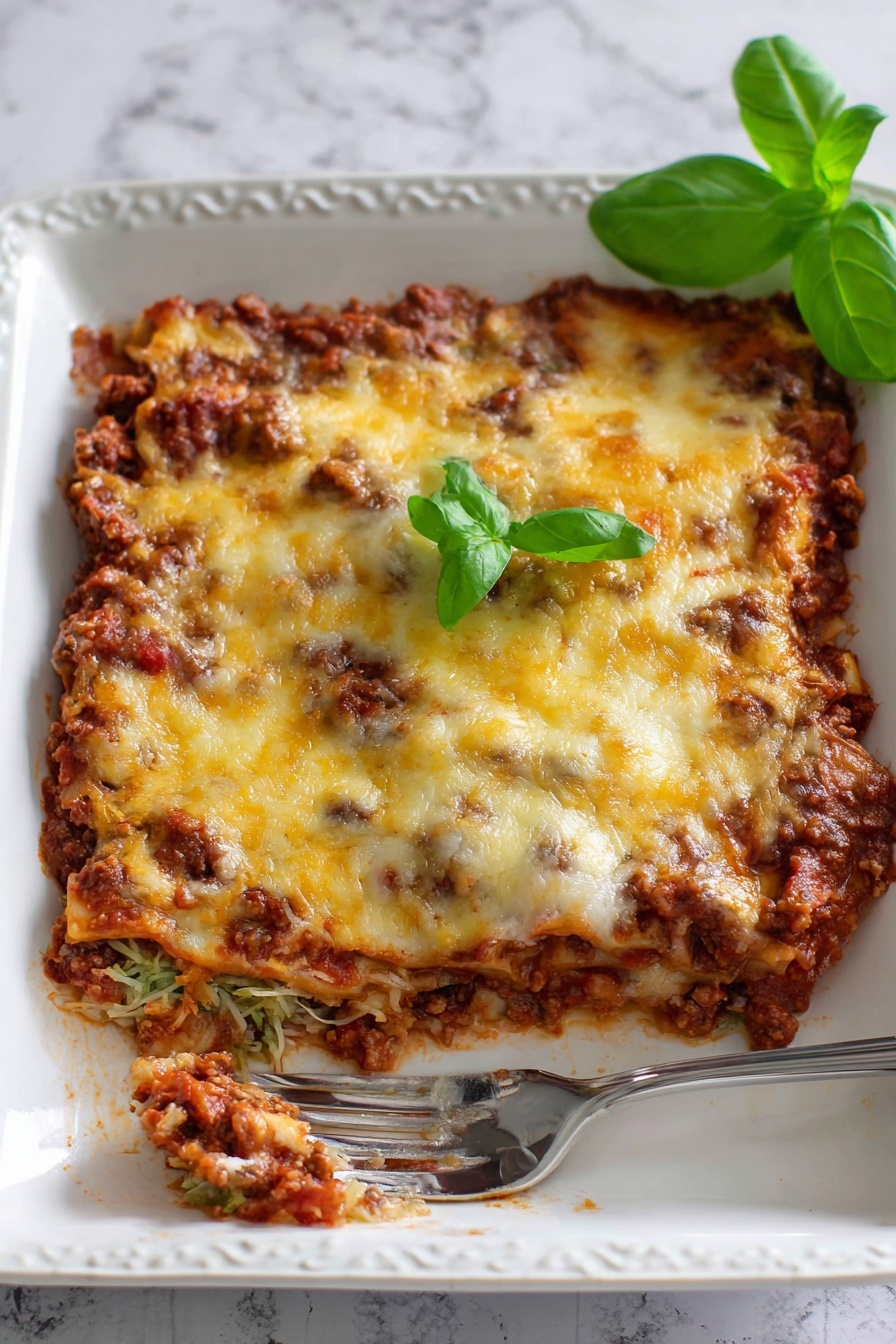 Zucchini Pizza Casserole, zucchini casserole with pizza flavors, healthy zucchini pizza bake, cheesy zucchini casserole, vegetable-packed pizza casserole - The image shows a white rectangular baking dish filled with a baked casserole that has three visible layers. The bottom layer is a chunky, dark brown meat sauce mixed with red tomato sauce creating a textured base. The middle layer is mostly hidden but looks to be another portion of meat sauce. The top layer is melted cheese with a mix of pale white and golden yellow colors, slightly browned in spots. Small green basil leaves are scattered on top, adding color contrast. In the bottom left corner, a metal spatula with a white handle is partially inserted under the casserole, revealing the inside layers and the rich texture of the dish. The dish is set on a white marbled surface. Photo taken with an iphone --ar 2:3 --v 7