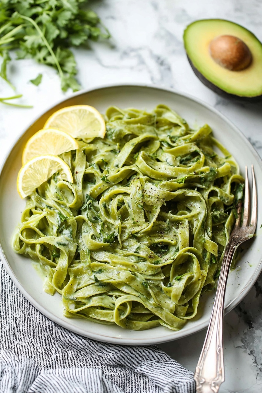 Avocado Lemon Pesto, healthy avocado pesto, quick vegan pesto, creamy lemon pesto, nut-free pesto - A clear blender jar with four sharp blades at the bottom contains a thick, smooth mixture of bright green color with a slight creamy texture. The blender base beneath is black with a large round silver knob in the center. The jar handle is transparent with a blue tint, positioned to the right, and the whole scene is set on a white marbled surface. photo taken with an iphone --ar 2:3 --v 7