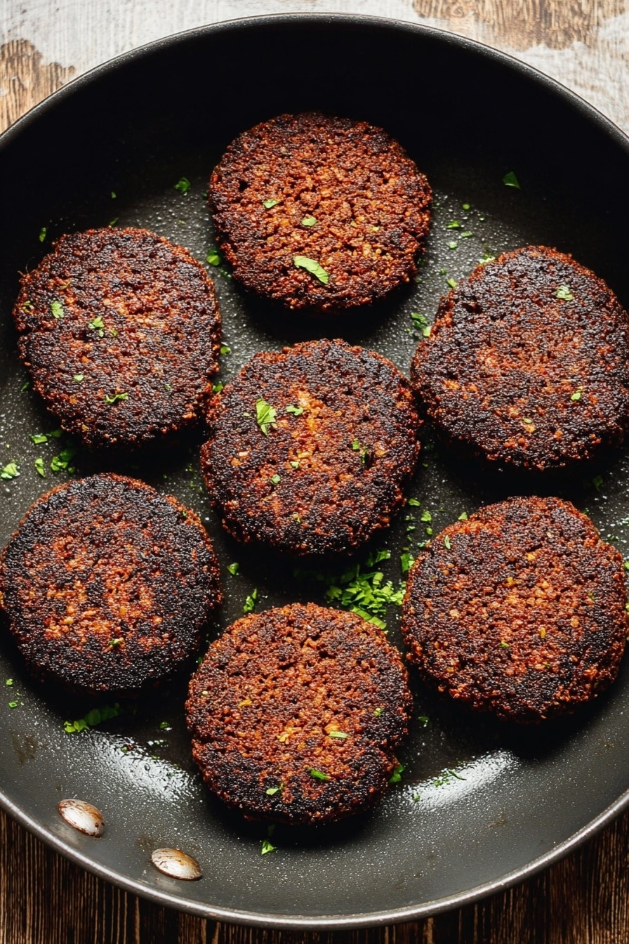 Vegan Breakfast Sausage, plant-based sausage recipe, vegan sausage breakfast ideas, homemade vegan sausage, savory vegan breakfast options - The image shows eight dark brown, crispy patties arranged evenly inside a black round pan. The patties have a coarse texture with some small bits visible, and are sprinkled lightly with small green herb pieces. The background surface seen at the top is wooden but will be imagined as a white marbled texture. The pan has a slightly shiny area where the light reflects. photo taken with an iphone --ar 2:3 --v 7