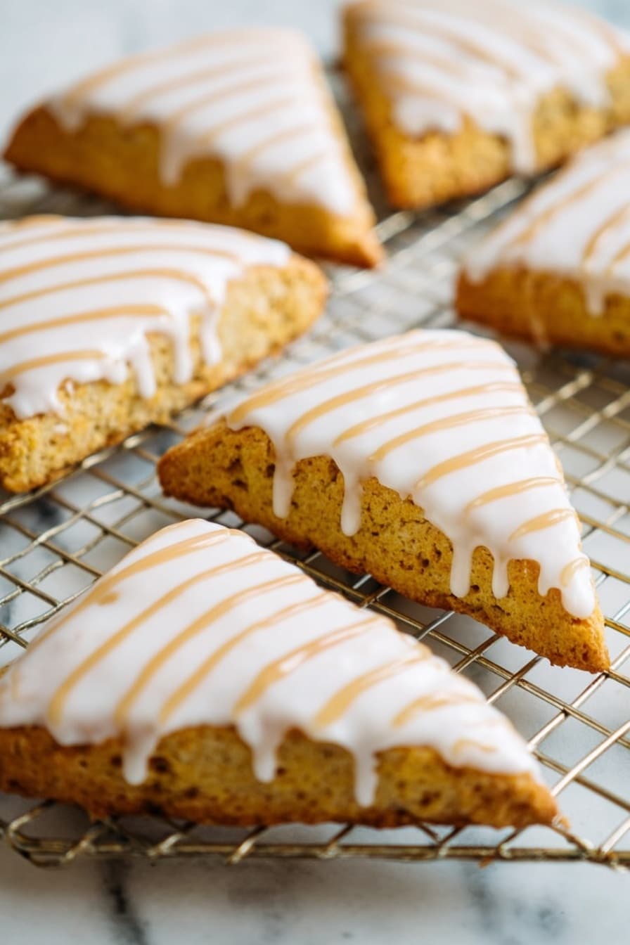 Starbucks Copycat Vegan Pumpkin Scones, vegan pumpkin scones recipe, vegan fall bakery ideas, homemade pumpkin scones, dairy-free pumpkin scones - The image shows a close-up of several triangular scones placed on a wire cooling rack over a white marbled surface. Each scone has a golden-brown, slightly rough texture base with a smooth, thick white icing layer covering the top. Over the white icing, there are thin, even lines of light brown drizzle arranged diagonally from one corner to the other. The scones are arranged in a casual pattern, filling the frame with their detailed textures and colorful toppings. photo taken with an iphone --ar 2:3 --v 7