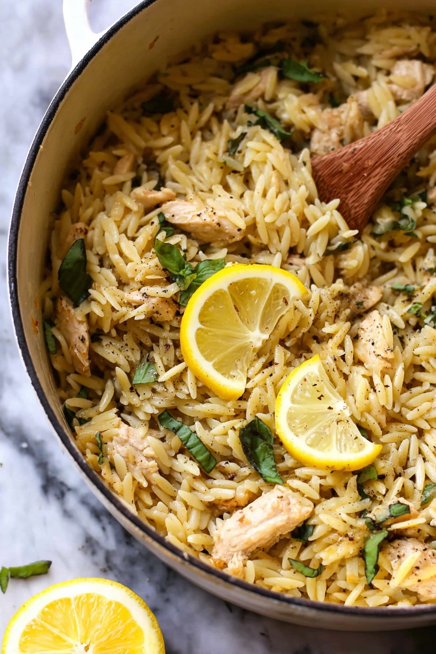 Lemon Chicken and Orzo, Lemon Chicken and Orzo recipe, easy lemon chicken with orzo, quick lemon chicken skillet, healthy lemon chicken dinner - The image shows a white pot filled with cooked orzo pasta mixed with small pieces of light brown chicken and fresh green basil leaves scattered throughout. Two bright yellow lemon slices rest on top as a garnish, and there are visible specks of black pepper sprinkled across the dish. A wooden spoon stirs the orzo on the right side, and a lemon wedge is blurred in the white marbled background. The texture of the orzo looks soft and slightly shiny, mixing well with the tender chicken pieces. photo taken with an iphone --ar 2:3 --v 7