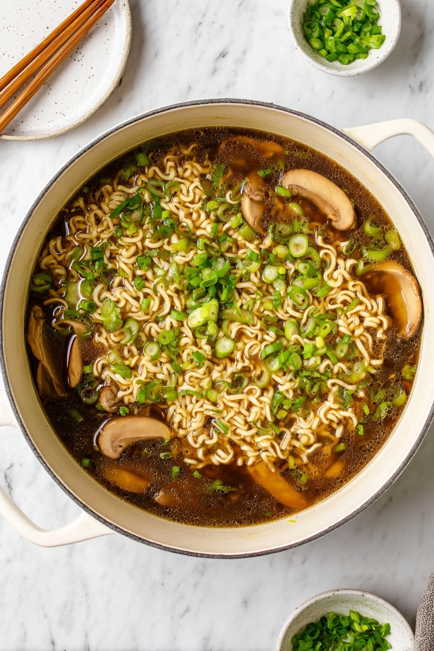 Easy Vegan Ramen, vegan ramen recipe, plant-based ramen, quick vegan soup, healthy vegan noodle bowl - A large white pot filled with dark brown broth containing light beige cooked curly noodles scattered throughout. Several slices of light brown mushrooms float on top, mixed with plenty of bright green chopped scallions spread evenly across the surface. The pot handles are visible on the sides, resting on a white marbled surface. In the background, a round white plate with wooden chopsticks rests towards the top left, and a small white bowl with extra chopped scallions sits on a matching saucer towards the top right. photo taken with an iphone --ar 2:3 --v 7