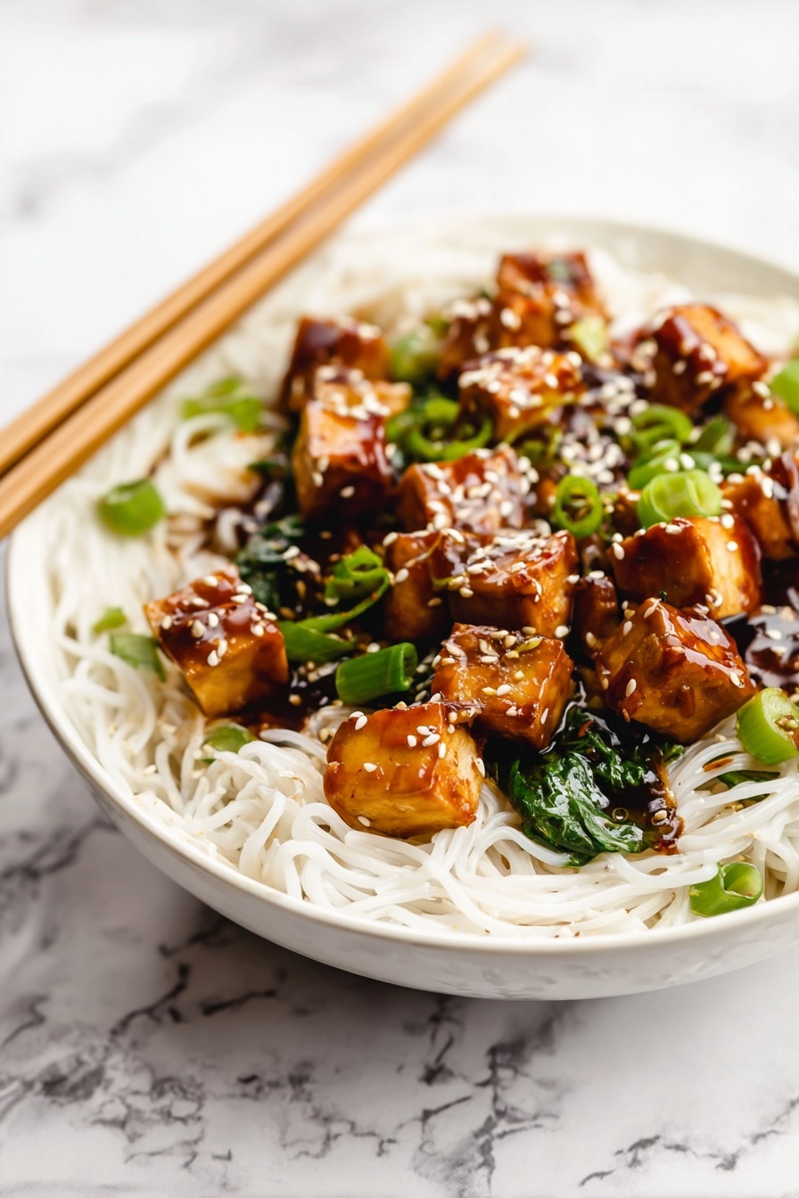 Quick One Pan Tofu Stir Fry, tofu stir fry, easy vegetarian dinner, healthy tofu recipe, quick weeknight dinner - A white bowl is filled with thin white noodles forming the base layer. On top, there are medium-sized golden brown tofu cubes coated in a shiny dark brown sauce. Bright green chopped scallions and spinach leaves are mixed in with the tofu. White sesame seeds are sprinkled over the tofu pieces, adding texture and color contrast. Wooden chopsticks rest on the edge of the bowl over a white marbled surface in the background. Photo taken with an iphone --ar 2:3 --v 7