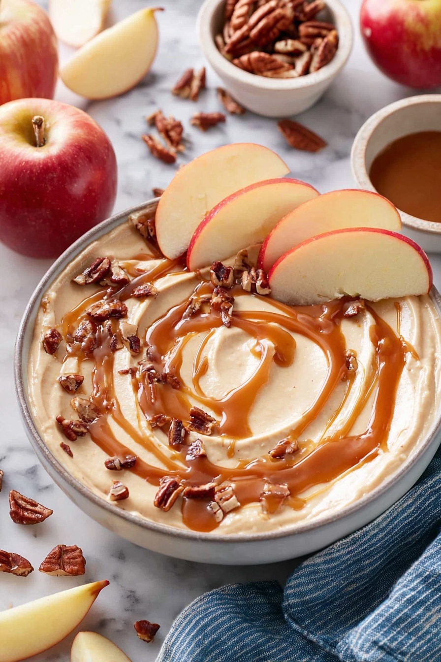 Caramel Cheesecake Dip, easy caramel cheesecake dip, creamy fruit dip, quick dessert dip, festive party dip - A white bowl filled with smooth, creamy light beige dip swirled on top, drizzled generously with rich caramel syrup in a circular pattern. Small pieces of chopped dark brown pecans are scattered over the dip, and slices of red apple with light yellow flesh are placed around the edge, some resting in the dip. In the background, whole and sliced apples and extra pecans are scattered on a white marbled surface, next to a small white bowl with more pecans and a small white bowl filled with caramel sauce. A blue-striped cloth is partially visible at the bottom right. Photo taken with an iphone --ar 2:3 --v 7