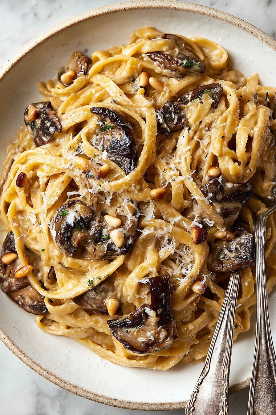 Caramelized Leek Mushroom Pasta, Leek Mushroom Pasta Recipe, Creamy Mushroom Leek Pasta, Vegetarian Pasta with Mushrooms, Gourmet Pasta with Gruyère - A white plate holds a dish of fettuccine pasta mixed with a creamy light brown sauce. The pasta strands are soft and twisted around each other, topped with several pieces of dark brown, slightly crispy mushrooms scattered on top and inside. Small tan pine nuts and grated pale yellow cheese are sprinkled evenly over the pasta. To the right side of the plate, two silver forks with delicate patterns rest partially on the pasta. The plate sits against a white marbled surface. Photo taken with an iphone --ar 2:3 --v 7