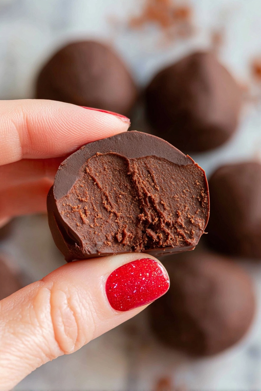 Healthy Chocolate Bean Energy Balls, healthy snack ideas, quick energy bites, vegan dessert recipes, guilt-free chocolate treats - A round white bowl filled with several smooth, shiny dark chocolate balls stacked together. Two of the chocolate balls are cut in half and placed on top, revealing a dense, rich, and slightly grainy brown chocolate filling inside. The bowl sits on a white marbled surface, giving a clean and bright look. The chocolate balls have a glossy outer layer with some small wrinkles, showing a contrast between the shiny dark coating and textured inside. Photo taken with an iphone --ar 2:3 --v 7