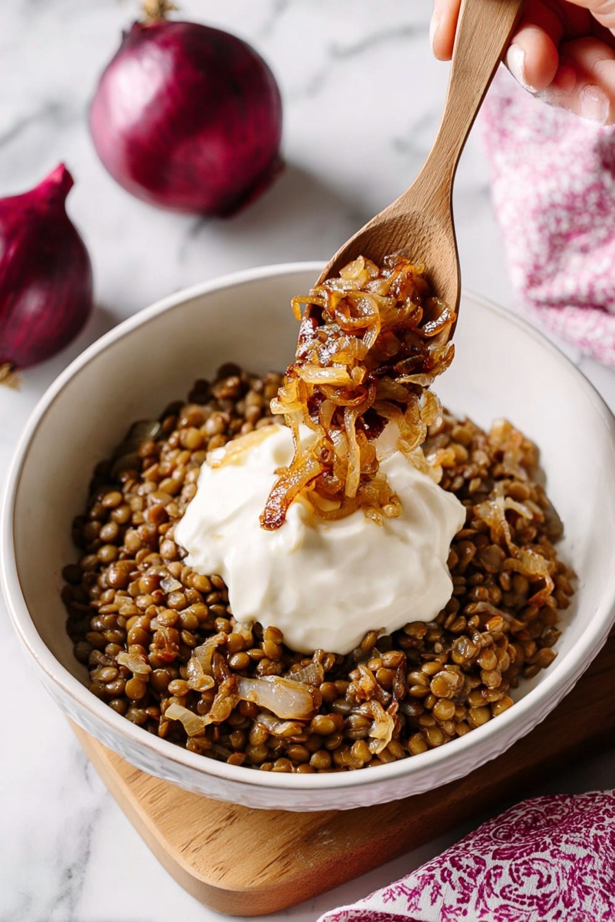 Easy Mujadara Lentils and Rice, Middle Eastern lentil and rice dish, hearty vegetarian meal, caramelized onion recipes, simple lentil recipes - A white bowl filled with a base layer of cooked lentils mixed with small pieces of caramelized onion, creating a brown and slightly textured bed. On top, there is a smooth, thick white dollop of sauce centered in the bowl. A wooden spoon is positioned above the bowl, held by a woman's hand, scooping some golden-brown caramelized onions over the sauce. The background features a white marbled surface with two whole red onions partially visible in the upper right corner and a softly blurred pink patterned cloth in the lower right. photo taken with an iphone --ar 2:3 --v 7