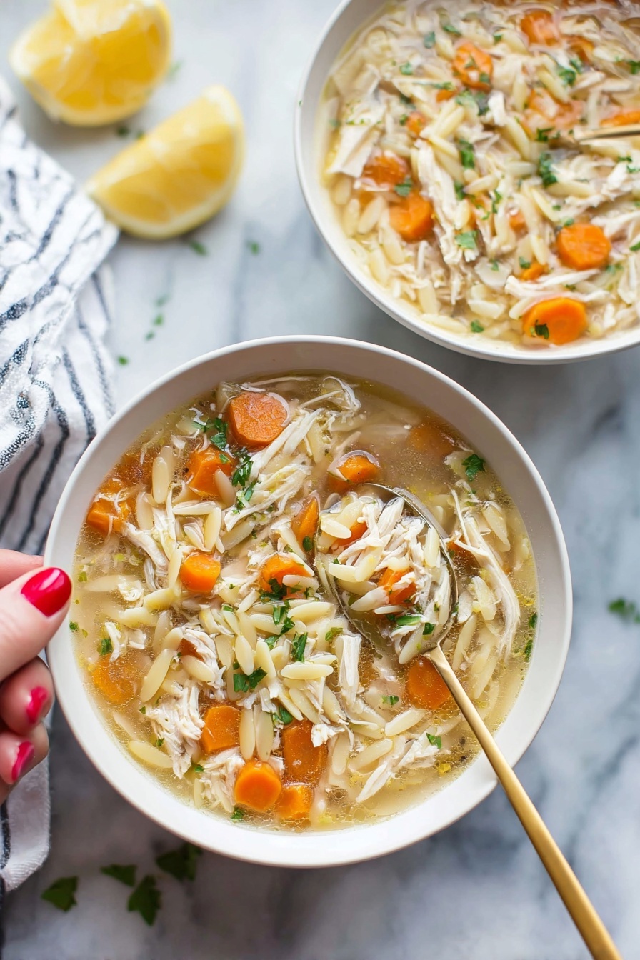 Lemon Chicken Soup with Orzo, Lemon Chicken Soup, Chicken and Orzo Soup, Bright Chicken Soup, Comforting Lemon Soup - Two white bowls filled with soup sit on a white marbled surface, each bowl holding a mix of shredded light brown chicken, small round orange carrot slices, and pale yellow orzo pasta floating in a light broth. Bright green herbs are sprinkled throughout the soup, adding fresh color. A gold spoon is held by a woman's hand with red painted nails, lifting a spoonful of soup from the bowl in the front, showing a clear view of the ingredients. In the background, a lemon half and a white-and-blue striped cloth are softly out of focus. photo taken with an iphone --ar 2:3 --v 7