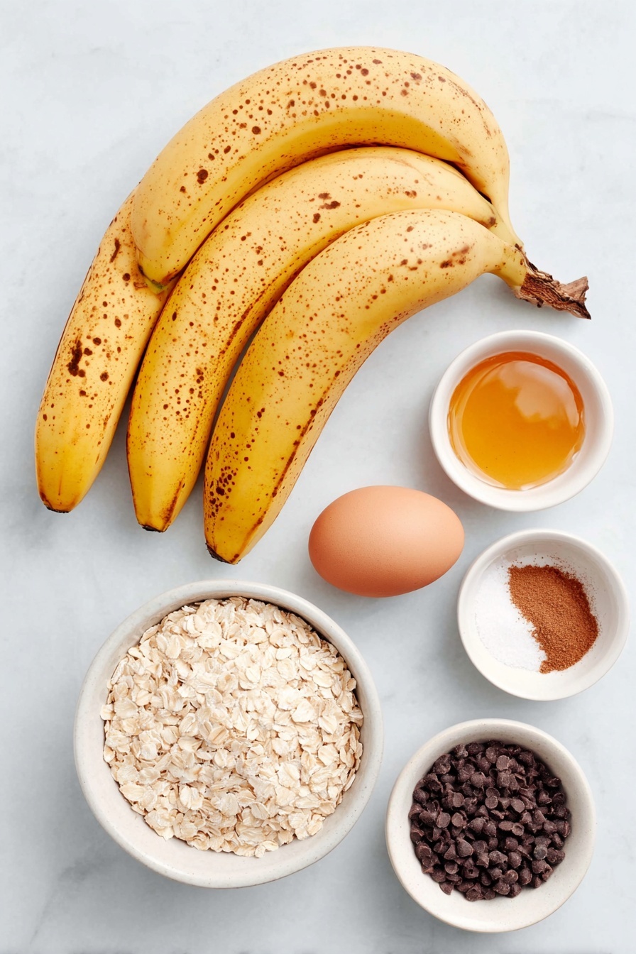 Banana Oatmeal Cookies, healthy banana cookies, easy oatmeal cookies, nutritious banana cookies, quick breakfast cookies - Flat lay of three overripe yellow bananas with brown spots, a small white ceramic bowl of golden honey, one whole uncracked brown egg, a small white ceramic bowl filled with quick cooking oats, a small white ceramic bowl containing ground cinnamon powder, a small white ceramic bowl of fine sea salt, and a small white ceramic bowl holding dark chocolate chips, all arranged with perfect symmetry and balanced proportions placed on a clean white marble surface, soft natural light, photo taken with an iPhone, professional food photography style, fresh ingredients, white ceramic bowls, no bottles, no duplicates, no utensils, no packaging --ar 2:3 --v 7 --p awthu7i m7354615311229779997