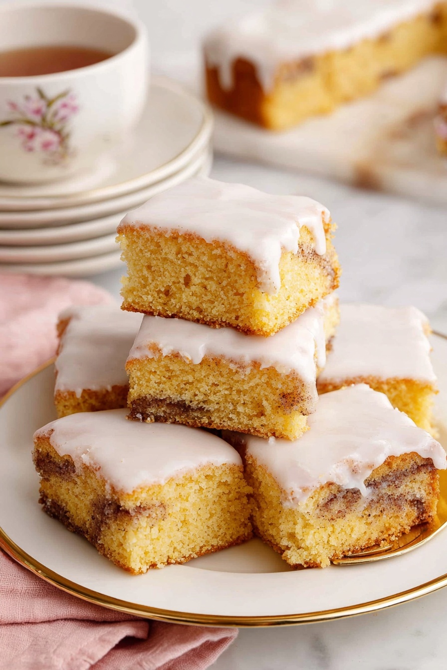 Cinnamon Roll Cake, easy cinnamon roll cake, moist cinnamon cake, cinnamon swirl dessert, quick cinnamon roll treat - The image shows a close-up of a square piece of cinnamon roll cake with three layers: a light golden brown cake base with swirls of dark cinnamon running through the middle, topped with a thick, white creamy icing that smoothly covers the top and slightly drips down the sides. The piece sits on a small, white plate with delicate floral and butterfly decorations and a thin gold rim. In the background, there is a white plate with several more pieces of the same cake stacked slightly on top of each other. To the right, a white teacup with a gold rim and small bee design is filled with dark tea. A gold fork lies on a soft pink cloth to the side, and all items rest on a white marbled textured surface. photo taken with an iphone --ar 2:3 --v 7