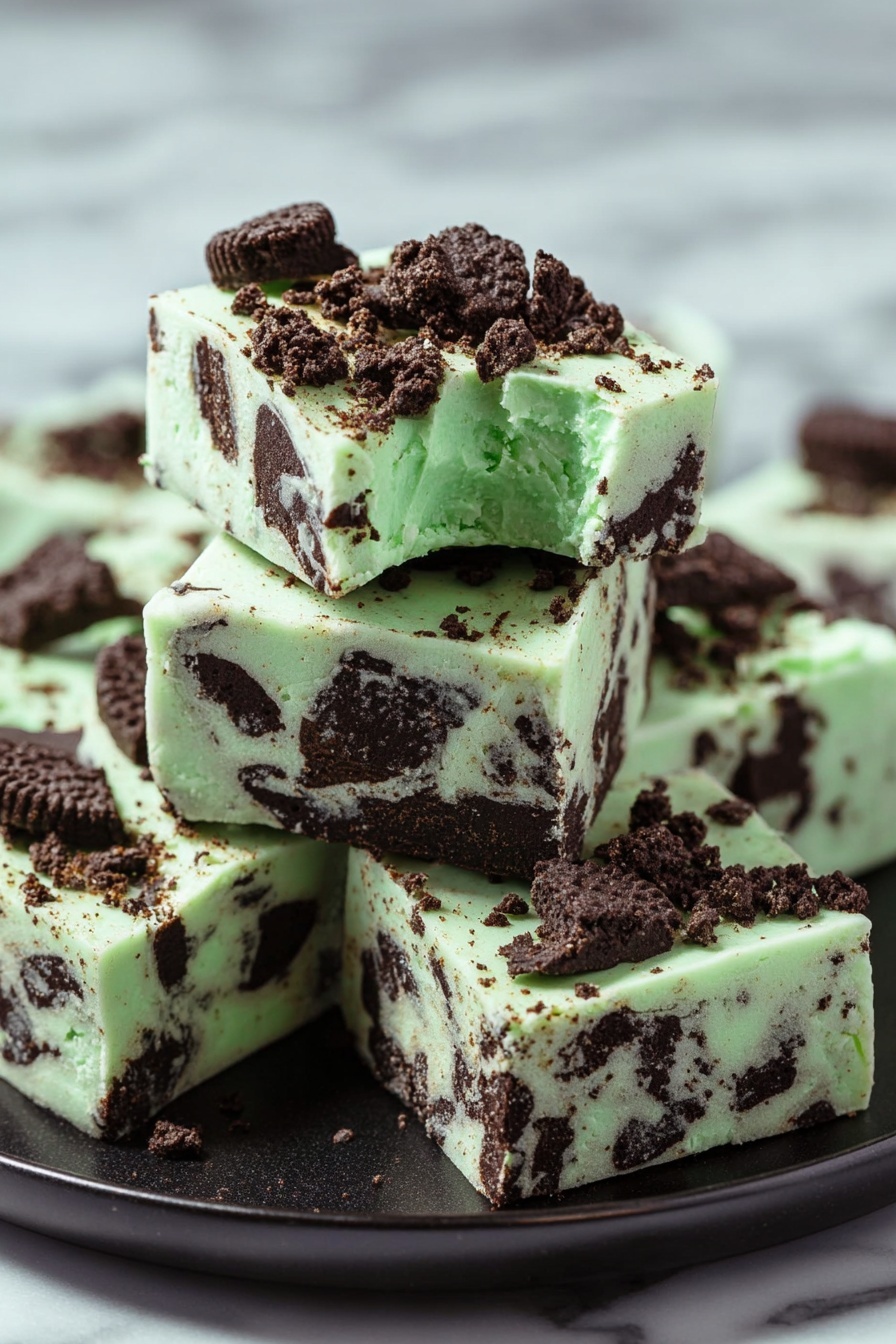 Mint Oreo White Chocolate Fudge, easy mint fudge recipe, no-bake Oreo fudge, white chocolate mint dessert, homemade holiday fudge - The image shows a stack of five square pieces of mint chocolate fudge on a black plate, placed on a white marbled surface. The fudge has a pale green base with dark brown chunks of cookie mixed in all layers. On the top, bigger cookie pieces and crumbs are scattered, adding texture and color contrast. Each piece is thick and smooth with distinct edges, and the top piece has a small bite taken from its corner, showing a creamy interior with visible cookie pieces inside. Photo taken with an iphone --ar 2:3 --v 7