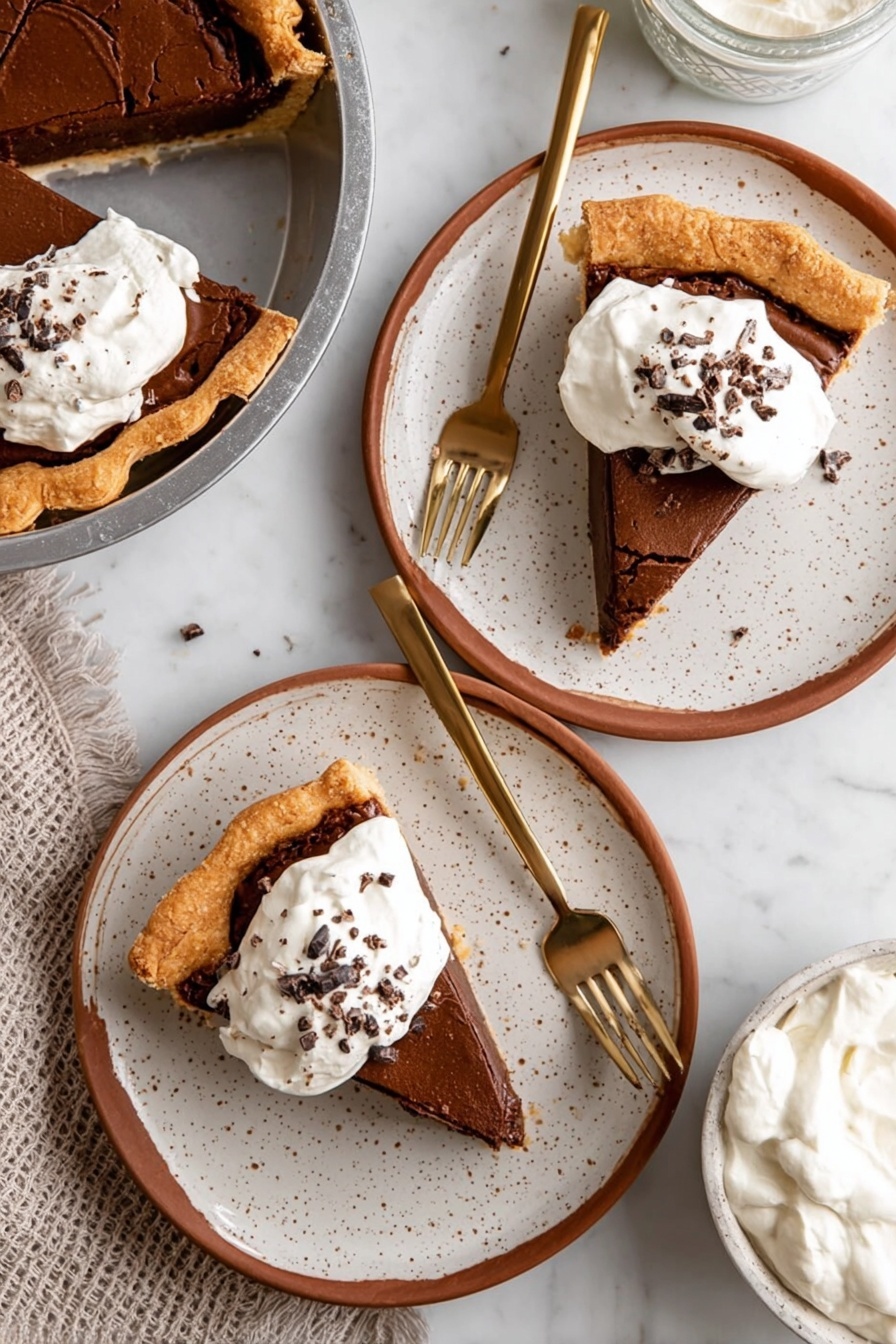 Fudgy Chocolate Brownie Pie, Chocolate Brownie Pie, Best Brownie Pie, Easy Brownie Pie, Chocolate Dessert - A slice of chocolate pie with three visible layers sits in a metal pie pan: the bottom layer is a light golden flaky crust, the middle layer is a thick dark brown chocolate filling, and the top layer is a cracked lighter brown chocolate crust. On top of the slice is a dollop of white whipped cream sprinkled with small chocolate shavings. The pie pan rests on a metal cooling rack over a white marbled surface. In the background, there is a blurred white container and a white bowl with more chocolate pie. photo taken with an iphone --ar 2:3 --v 7