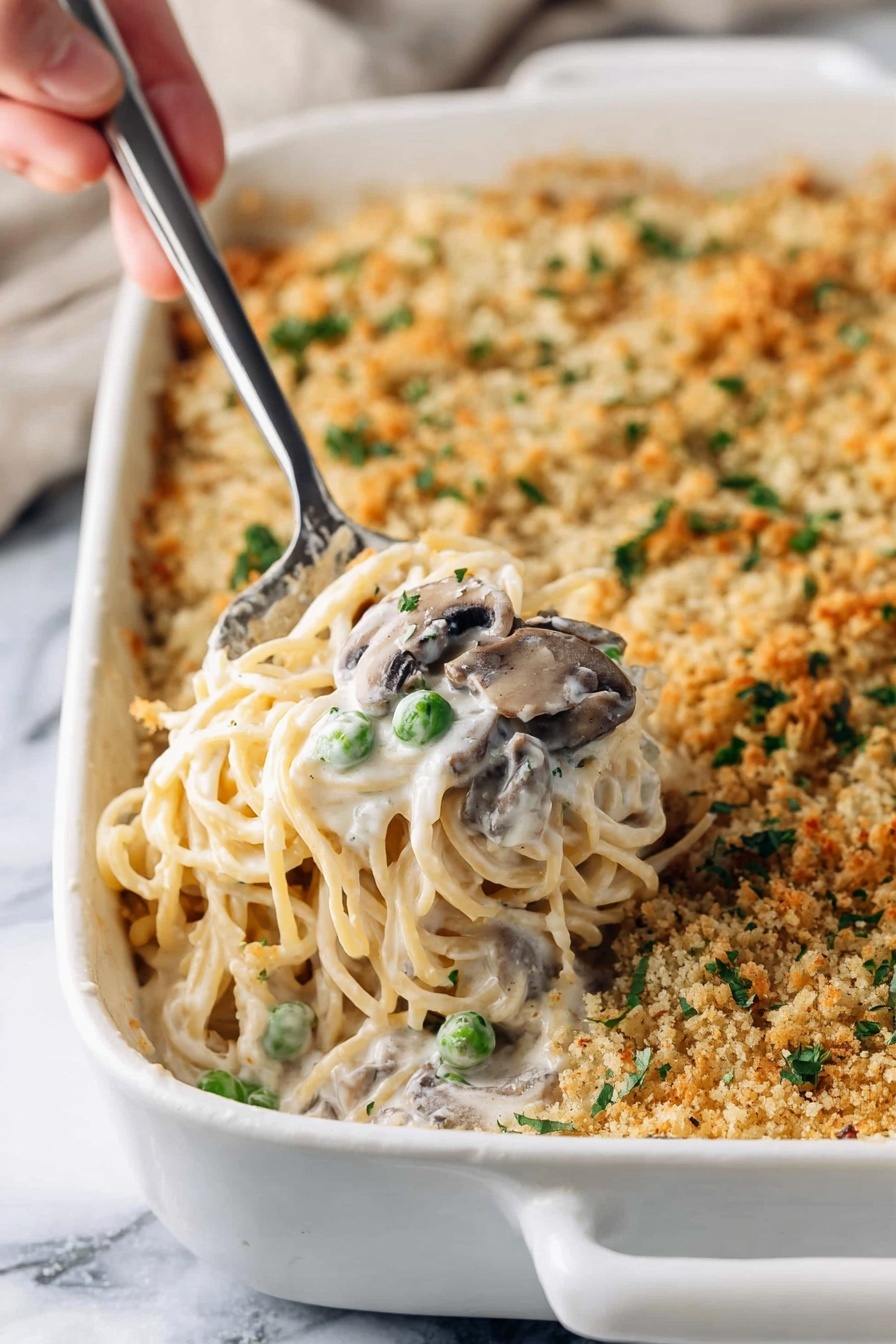 Creamy Turkey Mushroom Tetrazzini, turkey pasta bake, comforting pasta casserole, creamy mushroom sauce, leftover turkey recipes - A white baking dish filled with creamy spaghetti casserole topped with a golden brown crumb layer that has small green herb pieces sprinkled on it; a woman's hand holds a metal serving spoon lifting a portion showing soft spaghetti noodles mixed with white cream sauce, green peas, and sliced mushrooms, all nestled in the middle of the dish; the white marbled surface beneath adds a clean contrast to the warm colors of the casserole, photo taken with an iphone --ar 2:3 --v 7
