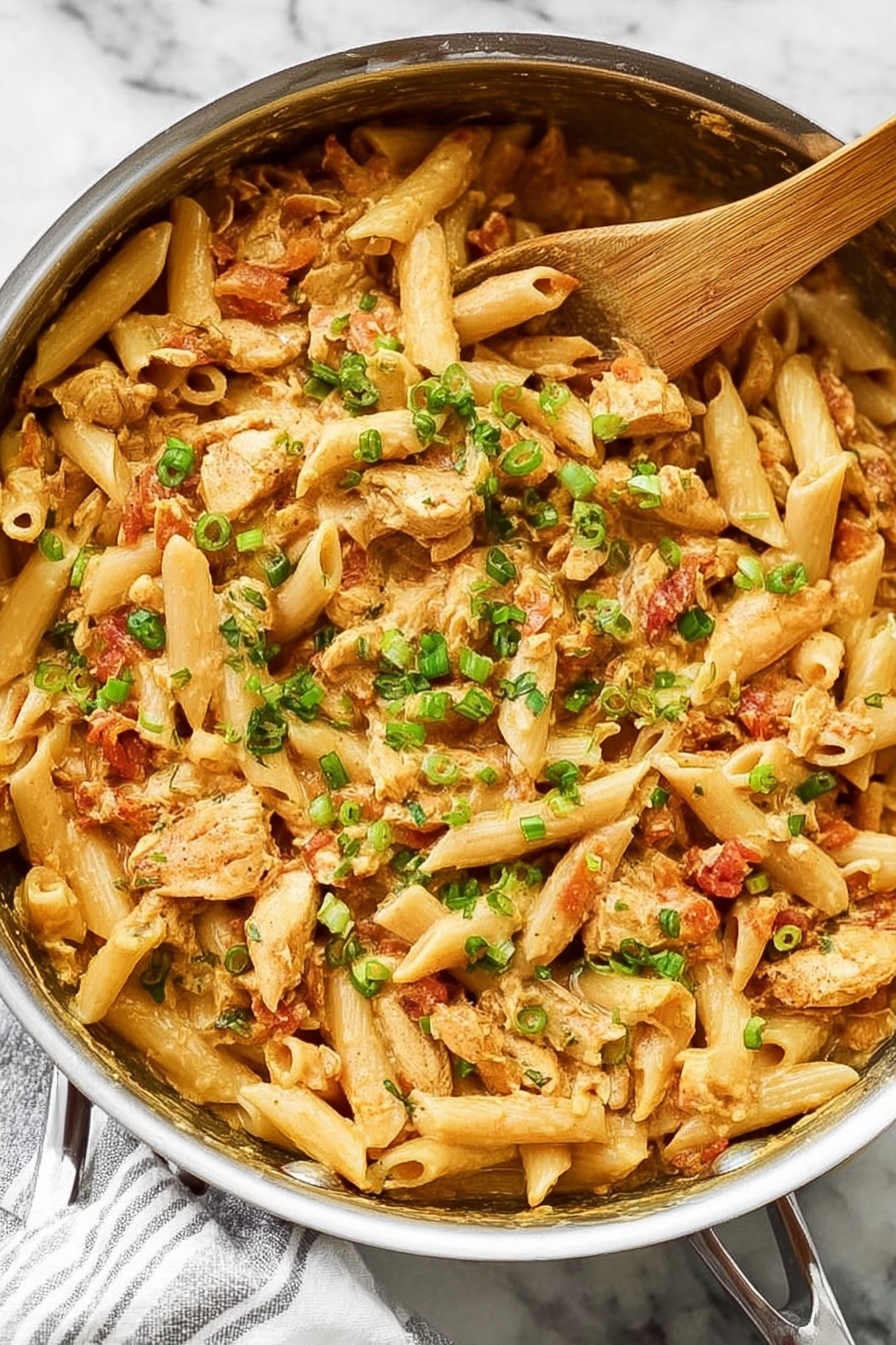 Creamy Cajun Chicken Pasta, Cajun Chicken Pasta, Creamy Pasta Recipes, Spicy Chicken Pasta, Easy Dinner Ideas - A close-up view of a large silver pan filled with creamy pasta made with short tube-shaped noodles, chopped light brown cooked chicken pieces, and a rich tan-colored sauce. Mixed in are small bits of red tomatoes and sprinkled chopped green onions on top to add bright green color contrast. A light wooden spoon rests inside the pan on the right side, partially covered by the pasta. The pan is placed on a white marbled surface with a white and gray striped cloth beneath the handle. The dish looks warm and inviting with a mix of soft textures and fresh garnish. Photo taken with an iphone --ar 2:3 --v 7