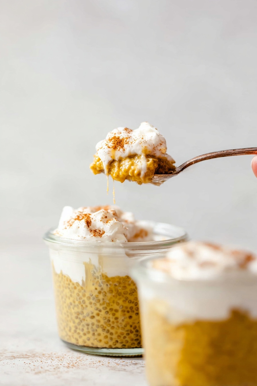 Pumpkin Chia Seed Pudding, healthy fall desserts, quick vegan pudding, nutritious breakfast ideas, cozy pumpkin snacks - The image shows a spoon holding a small scoop of a layered dessert with two clear glass jars filled with the same dessert in the background. The bottom layer in the jars is a yellowish-brown pudding with visible chia seeds, giving it a slightly bumpy texture. On top of the pudding is a thick, white cream layer lightly dusted with a brown spice, likely cinnamon. One jar has a woman’s hand partly visible holding a spoon covered with the white cream layer and some pudding drips on the rim. The background and surface are smooth with a white marbled texture. photo taken with an iphone --ar 2:3 --v 7