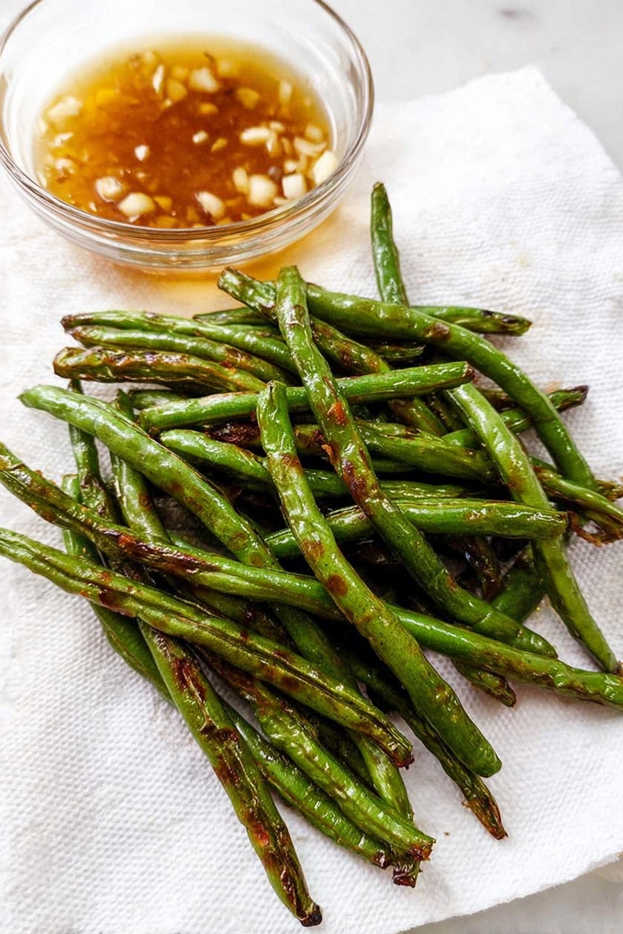 Garlic Green Beans Stir Fry, healthy green bean side dish, quick vegetable stir fry, garlic green bean recipe, easy green beans recipe - A close-up of cooked green beans piled loosely on a white plate, with each bean showing a shiny, slightly wrinkled green surface and some small pieces of browned garlic sprinkled on and around them. The beans have a mix of bright green and darker areas from cooking, and some beans are curved while others lay straight, creating a natural, uneven texture. The background is a white marbled texture. photo taken with an iphone --ar 2:3 --v 7