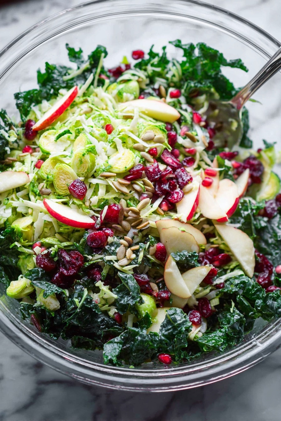 Shaved Brussels Sprouts with Pomegranate, Brussels Sprouts Salad with Pomegranate, Healthy Brussels Sprouts Salad, Christmas Brussels Sprouts Salad, Easy Brussels Sprouts Salad - A clear glass bowl filled with a fresh salad on a white marbled surface, showing multiple layers of ingredients. The base layer includes dark green leafy kale with a thick texture. On top, there is a layer of thinly sliced light green Brussels sprouts mixed with small slices of light red and white apple. Small pieces of red onion add specks of purple color throughout. Scattered across the salad are bright red dried cranberries and small shiny red pomegranate seeds. Light brown sunflower seeds are spread over the salad, adding texture. A silver serving spoon is partially visible inside the bowl. The whole scene is bright and fresh, with natural light highlighting the crispness of the vegetables and fruits. Photo taken with an iphone --ar 2:3 --v 7