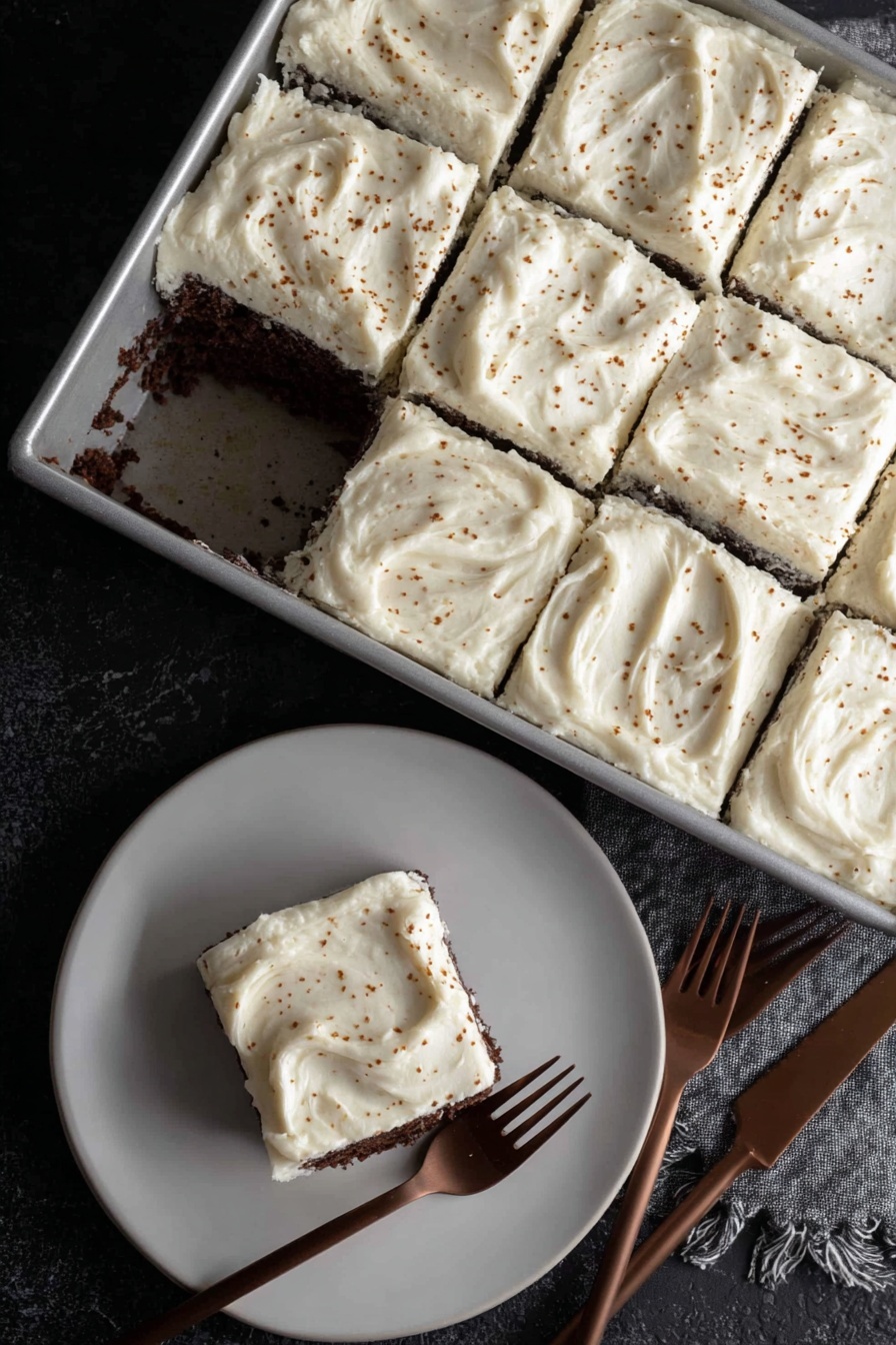 Dark Chocolate Espresso Cake with Brown Butter Frosting, chocolate espresso cake recipe, decadent chocolate cake with espresso, rich brown butter frosting, sophisticated cake dessert - A rectangular metal pan holds a cake cut into nine square pieces, with one piece missing near the center showing a dark, moist chocolate layer under a thick, creamy white frosting. Each frosting layer is spread thick and smooth with slight swirling patterns and small brown specks sprinkled over the top. On a white plate below, one square piece of the cake sits with the same thick white frosting on top and dark chocolate cake layer visible on the sides. Two brown forks lie near the plate on a black textured surface. photo taken with an iphone --ar 2:3 --v 7