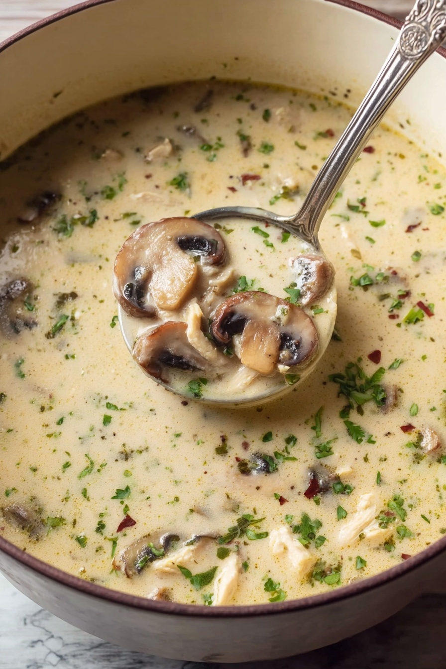 Creamy Chicken Mushroom Soup, comforting chicken and mushroom soup, velvety chicken mushroom soup, easy chicken mushroom soup recipe, hearty mushroom soup - A close-up view of a light creamy soup filled with sliced mushrooms and small pieces of chicken, sprinkled with chopped green herbs and tiny dried herbs throughout. The soup has a smooth texture with floating bits of green and brown, and a silver ladle scoops a portion showing three layers of sliced mushrooms, chicken bits, and the creamy broth all mixed. The soup is in a deep white bowl, resting on a white marbled surface. Photo taken with an iphone --ar 2:3 --v 7