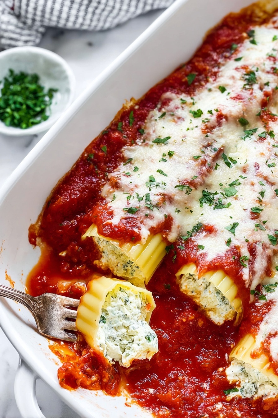 Easy Manicotti with Tomato Sauce, homemade manicotti, cheesy Italian pasta, simple Italian dinner recipe, comforting pasta dishes - The image shows a white rectangular baking dish filled with two rows of stuffed pasta shells, each covered with a layer of chunky red tomato sauce, melted white cheese, and sprinkled with fresh green herbs. The pasta shells are a pale yellow color with ridged edges visible beneath the sauce and cheese. Around the dish, on a white marbled surface, there are small bowls with green herbs and grated cheese, and some fresh red tomatoes on the vine. The overall look is warm and freshly baked with slight sauce splatters on the edge of the dish, photo taken with an iphone --ar 2:3 --v 7