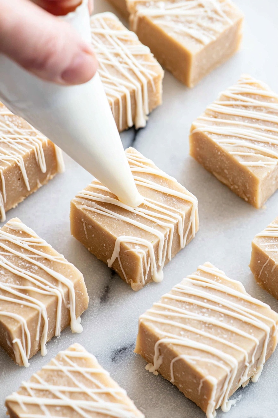 Cinnamon Roll Fudge, cinnamon roll fudge recipe, easy cinnamon fudge, white chocolate cinnamon fudge, cinnamon dessert ideas - Several small square pieces of light beige fudge with a smooth texture are placed on a white marbled surface. Each piece is being decorated with thin diagonal white icing lines that add contrast and a glossy look. A woman's hand holding a white piping bag is adding the icing in soft, even strokes, creating a neat, drizzled pattern across each fudge square. The fudge squares have slightly rounded edges and appear soft but firm. photo taken with an iphone --ar 2:3 --v 7