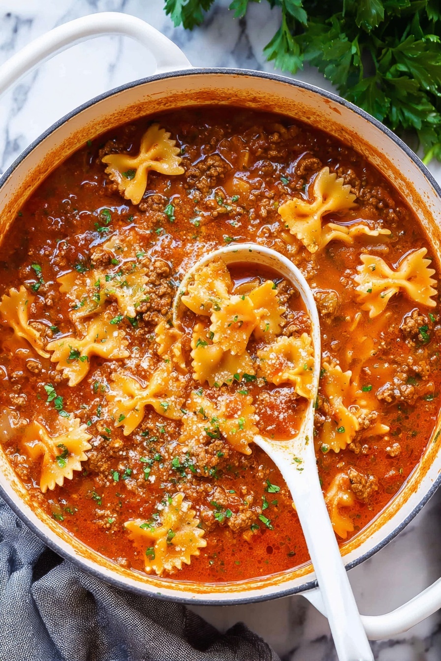 Lasagna Soup, easy lasagna soup, comforting soup recipes, quick weeknight dinners, Italian soup ideas - A large white pot filled with a rich, thick soup showing three main layers: a red tomato broth with a slightly oily surface, small chunks of brown cooked meat spread throughout, and pale orange bow-tie shaped pasta floating on top, sprinkled with small pieces of chopped green herbs. A white spoon is partly dipped in the soup revealing the sauce's thickness and layered textures. The pot is placed on a white marbled surface with some green herbs in the background and a gray cloth to the side, photo taken with an iphone --ar 2:3 --v 7