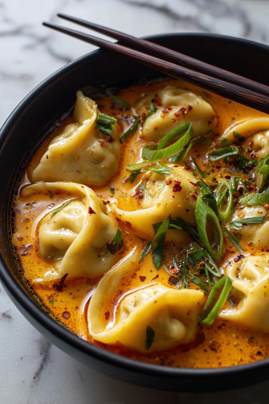 Coconut Curry Soup with Vegan Dumplings, vegan coconut curry soup, plant-based coconut curry, vegan dumpling recipes, creamy vegan curry soup - A close-up of six dumplings in a bowl filled with spicy orange-red broth, garnished with green sliced scallions and some red chili flakes sprinkled on top. The dumplings have a soft, pale yellow dough with a smooth texture and slightly folded edges. The bowl is black and round, sitting on a white marbled surface, and a pair of dark brown chopsticks rests on the bowl's edge, pointing diagonally away. The broth has little oil droplets and floating herbs giving it a rich texture and warm appearance photo taken with an iphone --ar 2:3 --v 7