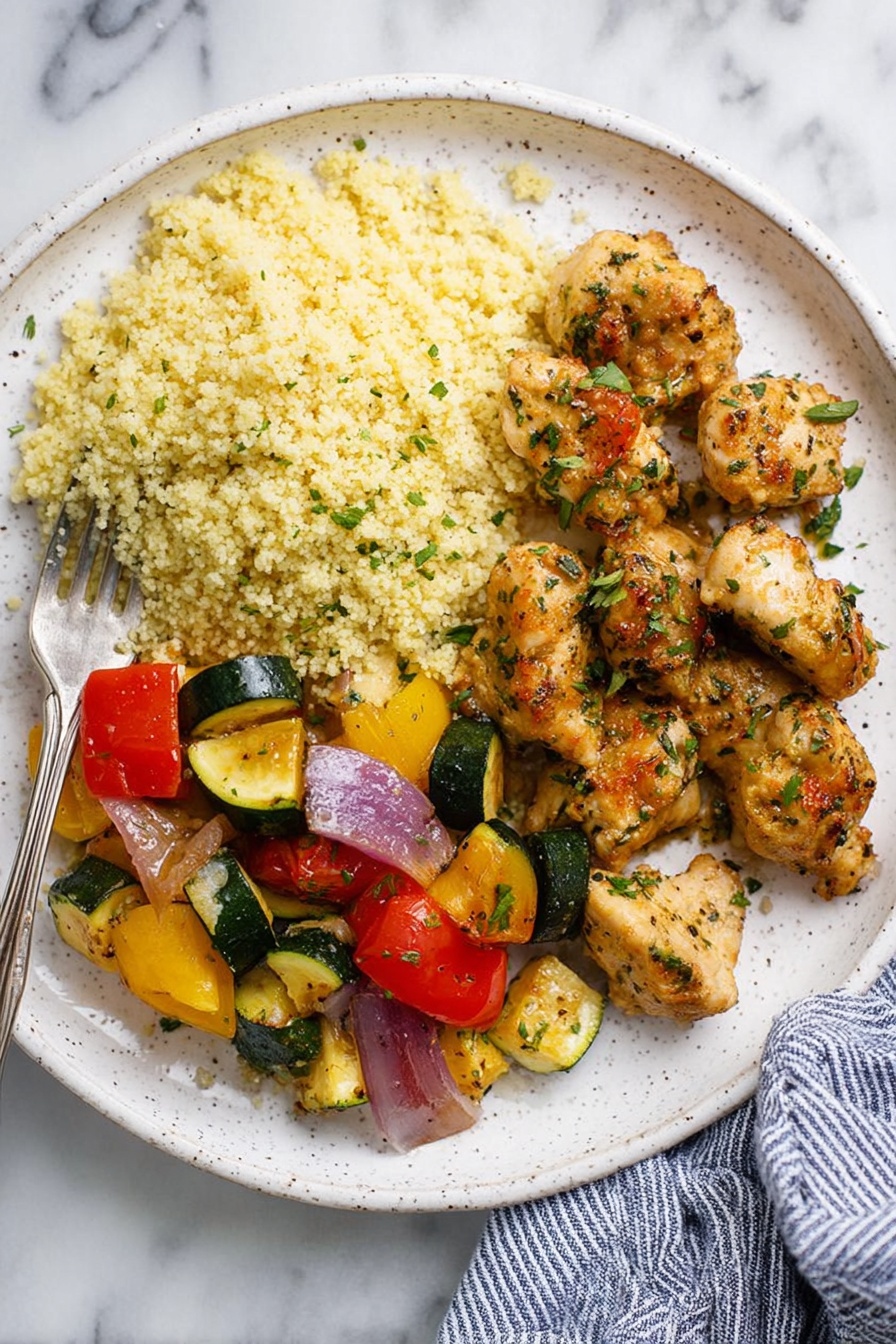 Garlic Butter Chicken Bites, crispy chicken bites, quick chicken recipes, easy garlic chicken, flavorful chicken dinner - The image shows a white speckled plate with three main parts: on the left, there is a light yellow couscous pile with a fluffy texture; on the bottom left, there is a mix of sautéed colorful vegetables including red tomatoes, green zucchini, yellow squash, and purple onion pieces, all slightly glossy; on the right side, there are several golden brown herb-seasoned chicken pieces, with a slightly crispy outside and specks of green herbs on them. A silver fork rests on the left edge of the plate, and the plate is placed on a white marbled surface with a blue and white striped cloth partially visible on the right side; photo taken with an iphone --ar 2:3 --v 7