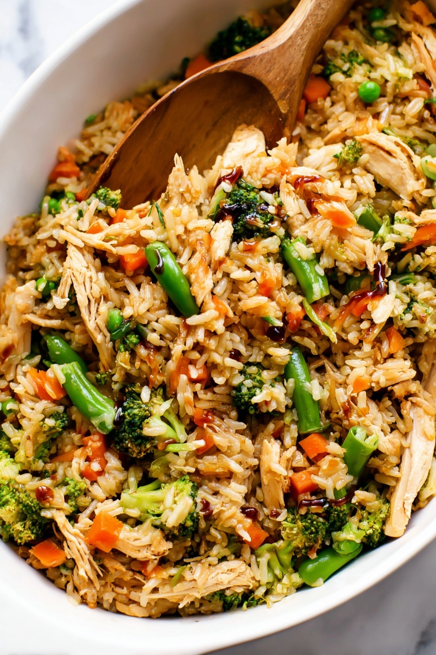 Teriyaki Chicken Casserole with Vegetables, healthy teriyaki chicken bake, easy chicken casserole recipe, flavorful vegetable chicken bake, quick weeknight dinner ideas - The image shows a close-up of a white dish filled with a colorful fried rice mix. The dish has multiple layers: the base layer is golden-brown cooked rice, mixed with small pieces of shredded light brown cooked chicken. Scattered throughout are bright green broccoli florets and snap peas, as well as vibrant orange baby carrots. The vegetables add texture and color contrast, while some parts of the rice have a glossy look from a dark soy sauce drizzled on top. A wooden spatula is partially buried in the mixture, lifting some of the rice and vegetables. The dish is placed on a white marbled surface. Photo taken with an iphone --ar 2:3 --v 7