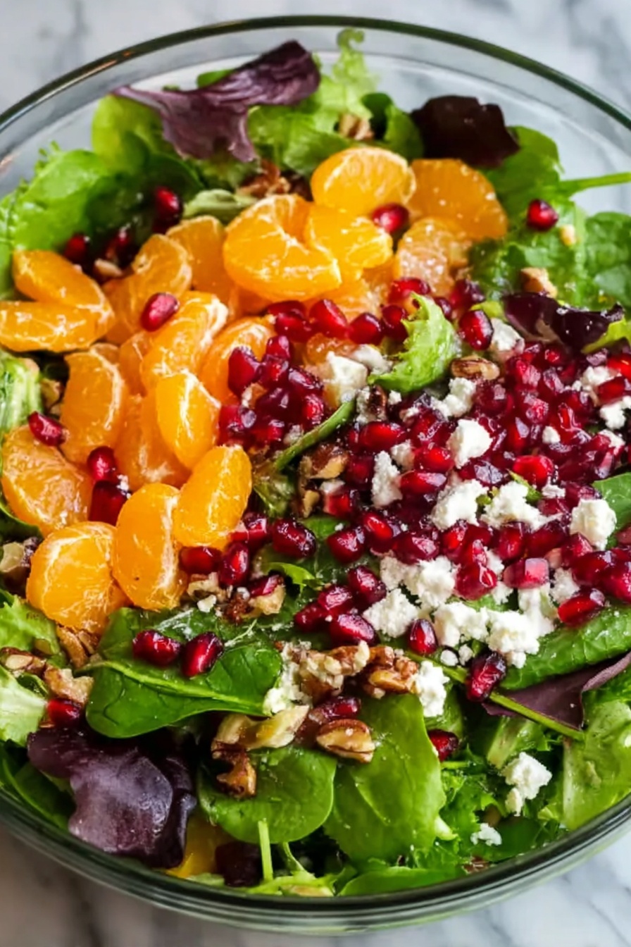 Fresh Winter Salad with Orange and Pomegranate, winter citrus salad, healthy winter salads, seasonal fruit salad, festive winter greens - A large clear glass bowl filled with a fresh salad containing several layers: at the bottom, a mix of green leafy spinach and lettuce with dark purple leaves, topped with bright orange mandarin slices scattered evenly. On top of this are small red pomegranate seeds sprinkled throughout, along with crumbled white cheese and small brown nut pieces. The colors are vivid and fresh, and the textures range from soft leaves to juicy fruit and crunchy nuts, all sitting on a white marbled surface. Photo taken with an iphone --ar 2:3 --v 7