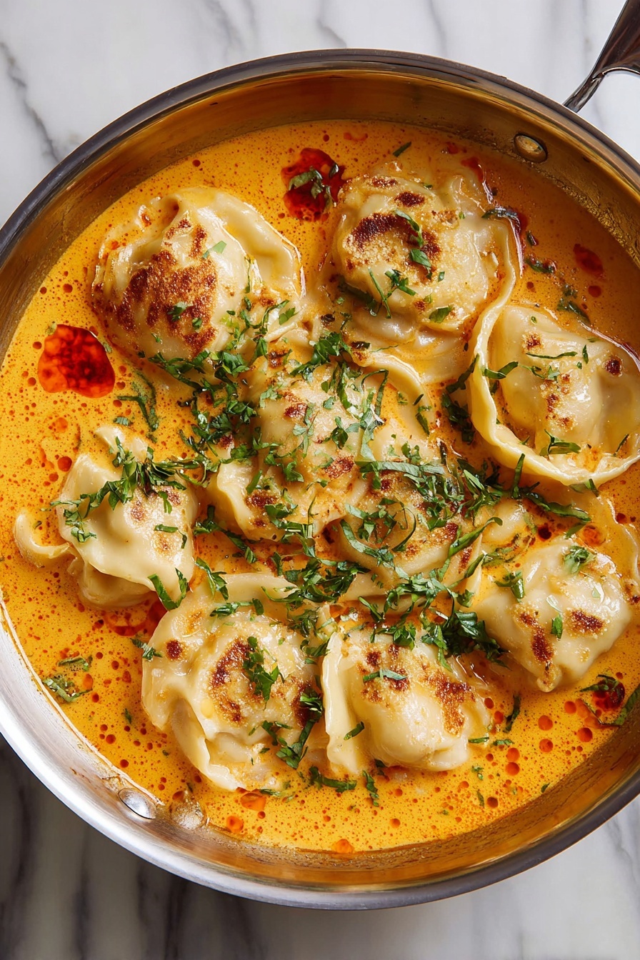 Coconut Curry Soup with Vegan Dumplings, vegan coconut curry soup, plant-based coconut curry, vegan dumpling recipes, creamy vegan curry soup - A shiny metal pan contains seven dumplings that are layered in a creamy orange sauce. The dumplings have a light beige color with some browned spots on top, showing slight crisp edges. The orange sauce has a smooth texture with small red oil droplets scattered across the surface. Fresh, chopped green herbs are sprinkled generously over the dumplings and sauce, providing a bright contrast. The pan is placed on a white marbled surface. Photo taken with an iphone --ar 2:3 --v 7