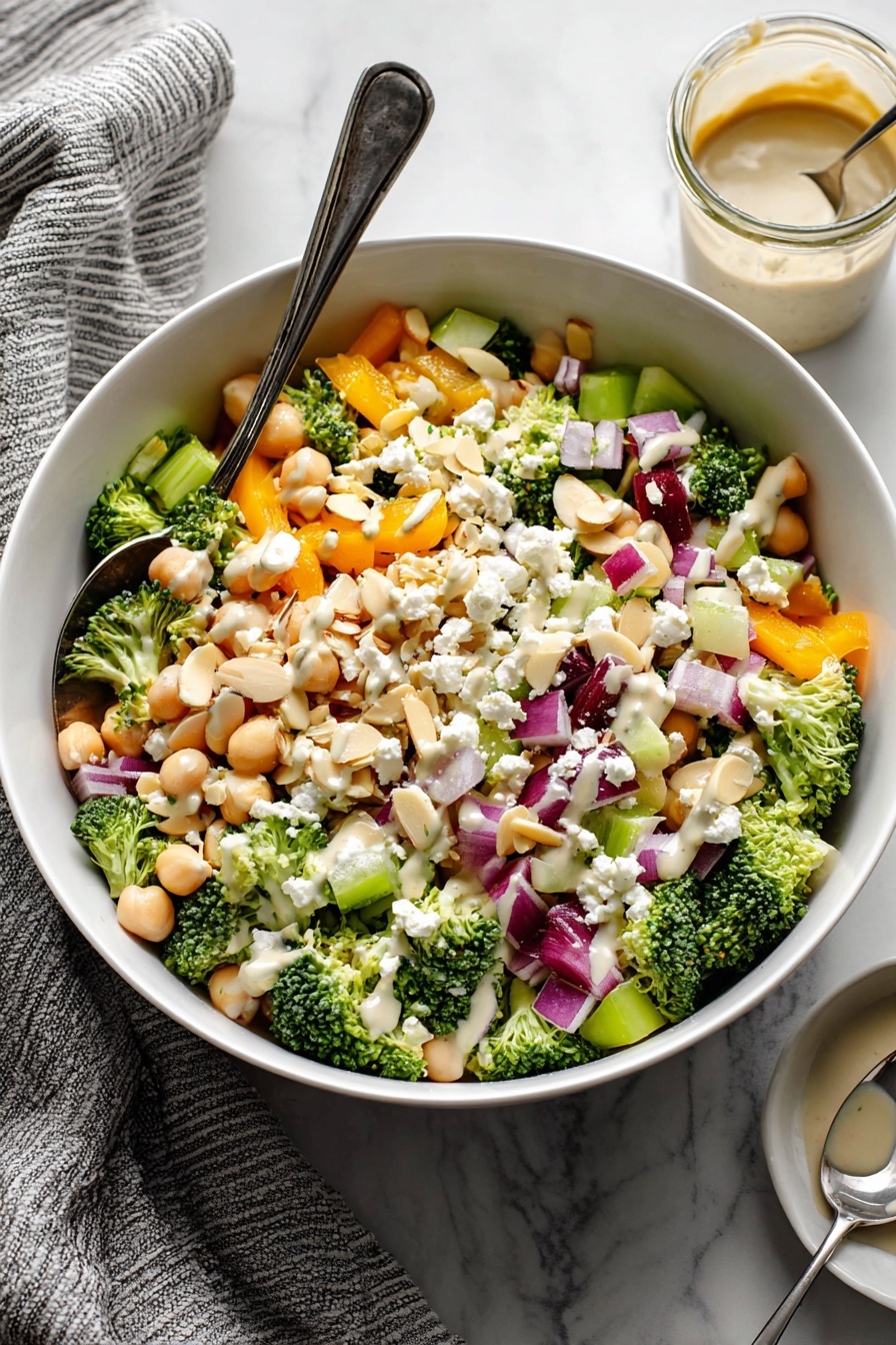 Broccoli Chickpea Salad with Lemon Tahini Dressing, healthy broccoli chickpea salad, lemon tahini dressing recipe, vegan salad ideas, easy veggie salad - A white bowl filled with a colorful salad showing multiple layers: the base layer consists of small, bright green broccoli florets and light beige chickpeas; scattered throughout are chunky orange bell pepper pieces and pale green celery bits; bright purple-red onion cubes are mixed evenly, adding contrast; white crumbled cheese pieces are sprinkled on top along with thin, light beige almond slivers; a light creamy dressing is drizzled over the salad, visible especially on the cheese and broccoli. A silver spoon rests in the bowl on the left side, and in the background there is a small glass jar with more dressing and a spoon inside it; the bowl is placed on a white marbled surface with a grey striped towel to the left. photo taken with an iphone --ar 2:3 --v 7