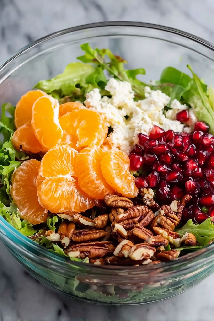 Fresh Winter Salad with Orange and Pomegranate, winter citrus salad, healthy winter salads, seasonal fruit salad, festive winter greens - A clear glass bowl holding a fresh salad on a white marbled surface, with a base layer of mixed green leaves. On one side are bright orange segments of peeled mandarins, stacked together. Next to the mandarins, crumbled white cheese is placed, adding a soft texture. Beside the cheese, there is a pile of small, glossy red pomegranate seeds. On the last side, a heap of chopped brown pecans adds a crunchy contrast. Photo taken with an iphone --ar 2:3 --v 7