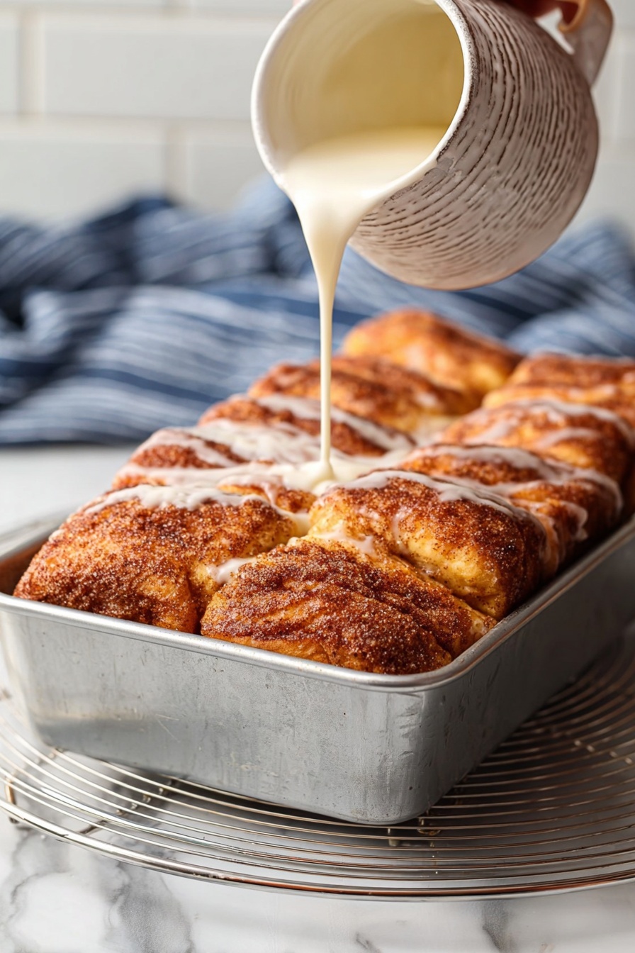 Cinnamon Sugar Bread, Cinnamon Sugar Bread Recipe, Soft Cinnamon Bread, Sweet Breakfast Bread, Easy Cinnamon Bread - The image shows two large cinnamon rolls on a round wire cooling rack over a white marbled surface. Each cinnamon roll has many layers of soft, golden-brown dough swirled with dark cinnamon filling, creating a textured look. On top, white icing is drizzled unevenly across the rolls, with some parts thicker and some parts thinner, making the rolls look moist and fresh. The background is bright and softly blurred, focusing attention on the rolls. photo taken with an iphone --ar 2:3 --v 7