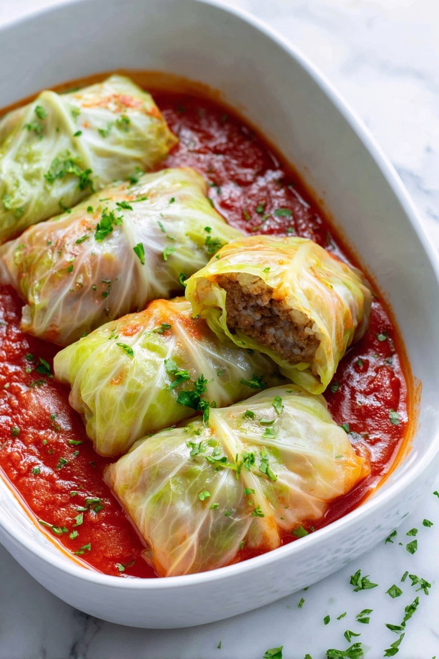 Savory Baked Stuffed Cabbage Rolls, stuffed cabbage rolls recipe, baked cabbage rolls, hearty cabbage roll dish, easy stuffed cabbage recipes - The image shows a white baking dish filled with ten cabbage rolls arranged neatly in two rows. Each cabbage roll is wrapped in pale green cabbage leaves that look soft and slightly glossy, with some light browning on edges. The cabbage rolls sit in a rich red tomato sauce that covers the bottom and comes up around the rolls. Small sprinkles of chopped green herbs are scattered over the rolls and sauce, adding color contrast. The dish is set on a white marbled surface with a white and blue striped cloth nearby and some green cabbage leaves partially visible in the background. photo taken with an iphone --ar 2:3 --v 7
